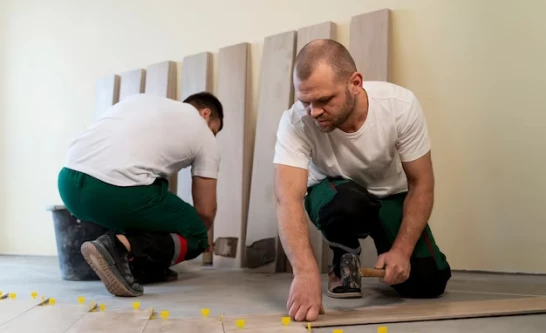 Image montrant deux hommes en train de travailler en posant du carrelage dans un bâtiment.